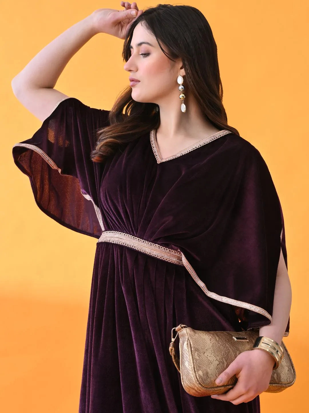 Woman in a dark purple dress with a gold clutch against an orange background