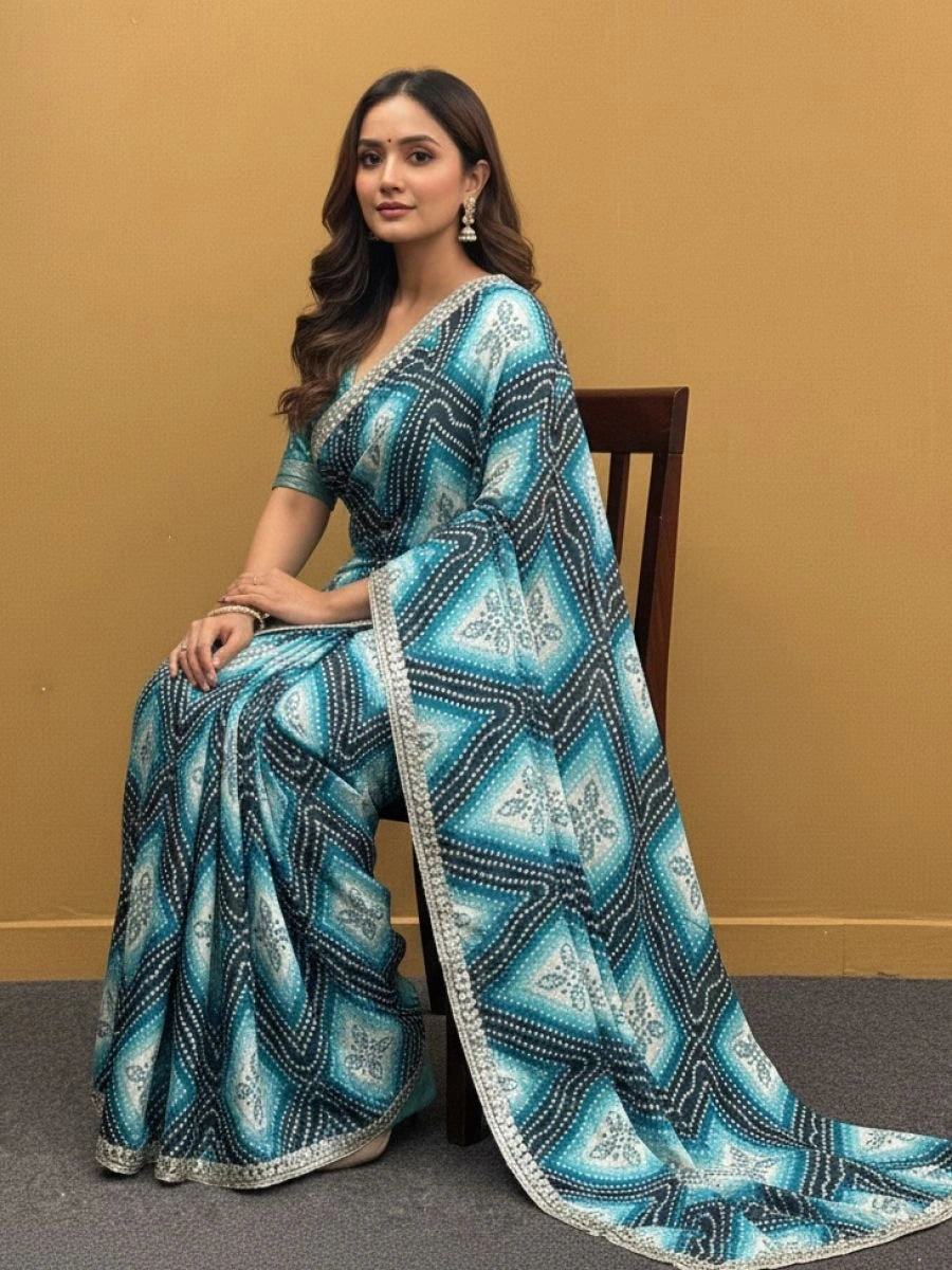 Woman wearing a blue and white patterned saree sitting on a chair against a beige wall.