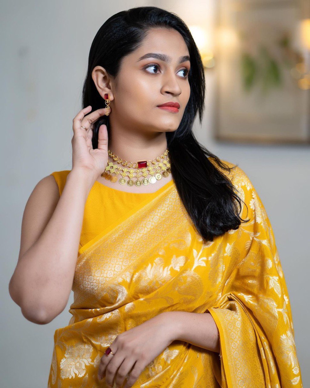 Woman wearing a yellow saree with gold jewelry indoors