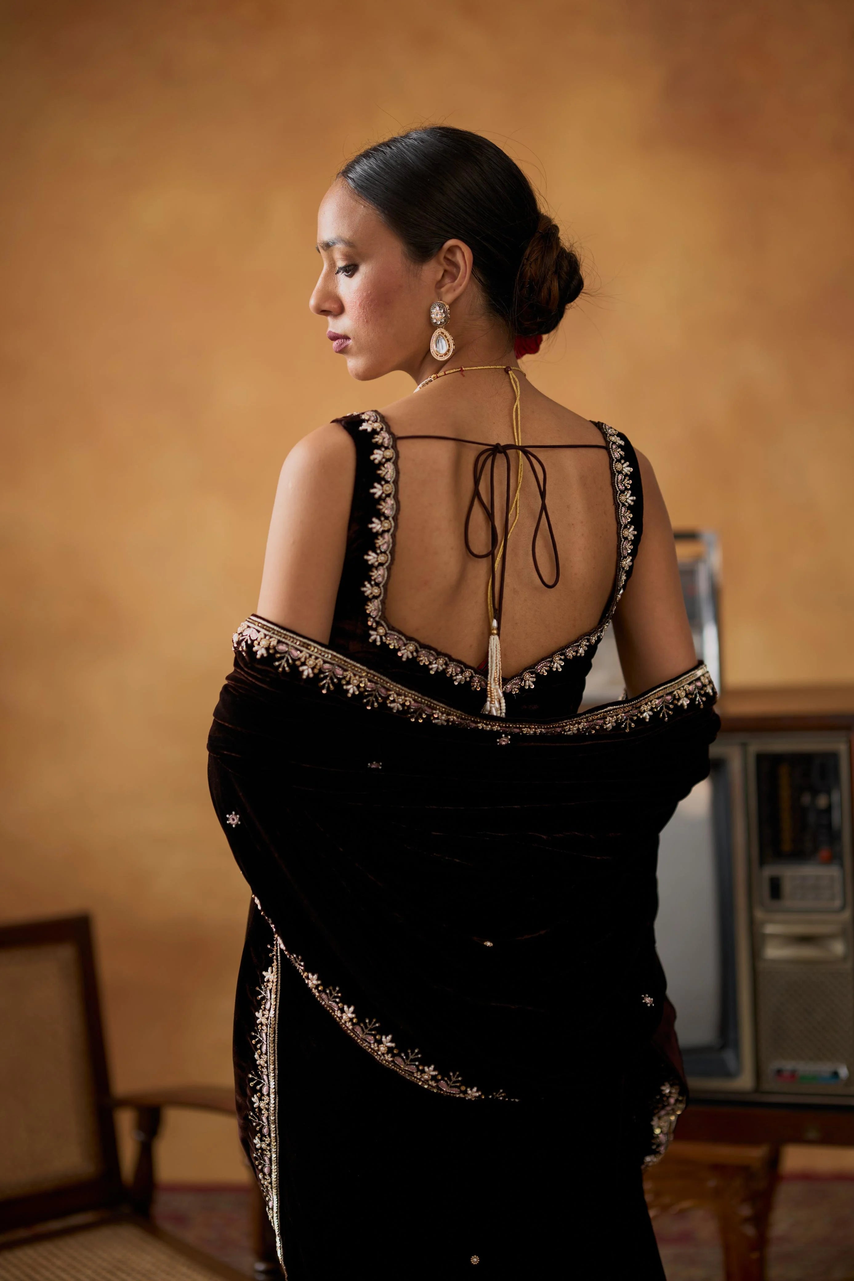 Woman wearing a black saree with intricate designs in a warm-toned room.