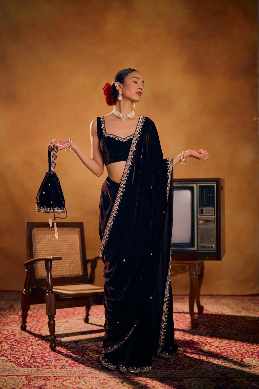 Woman in a black saree with a vintage television and chair in the background