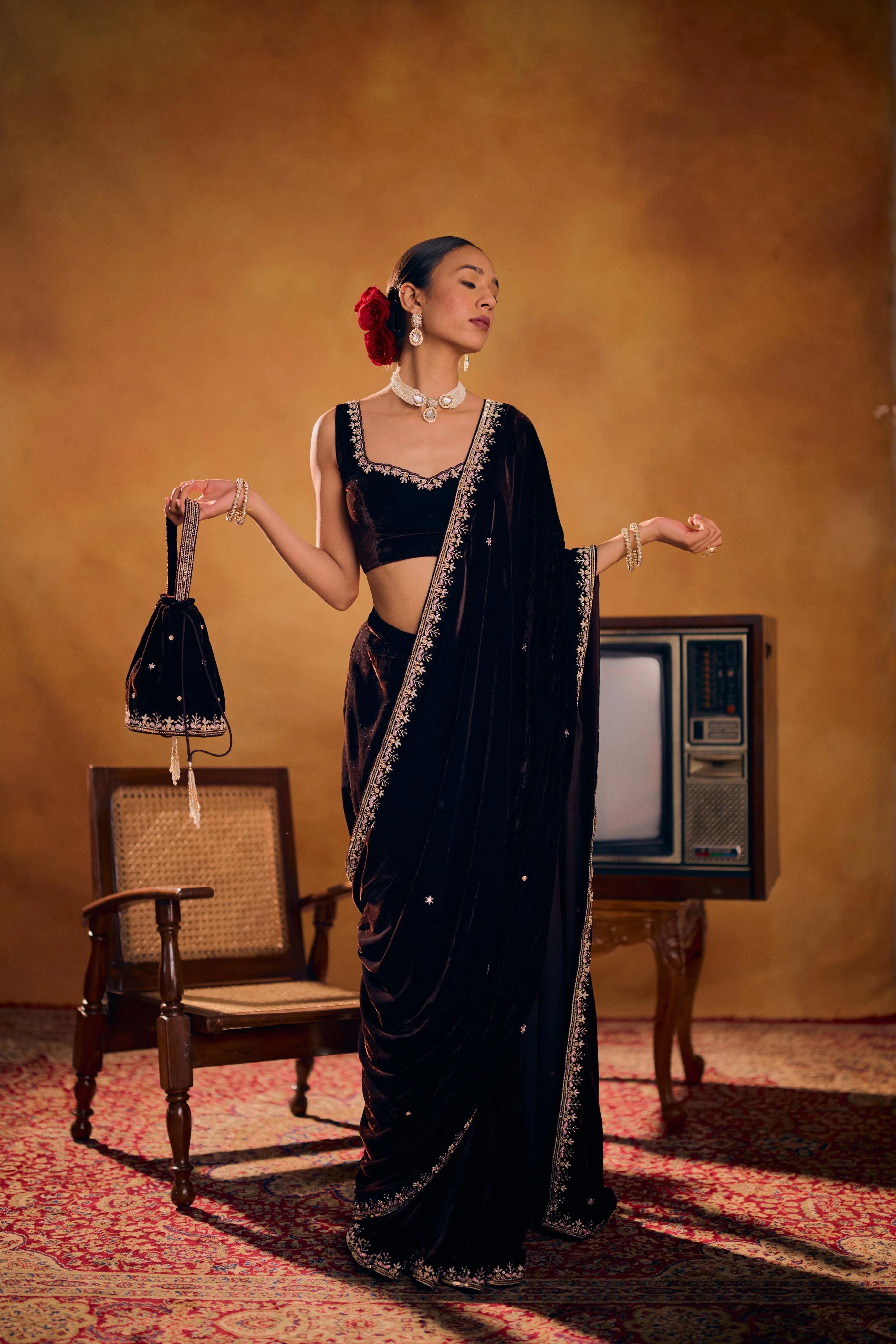 Woman in a black saree with a vintage television and chair in the background