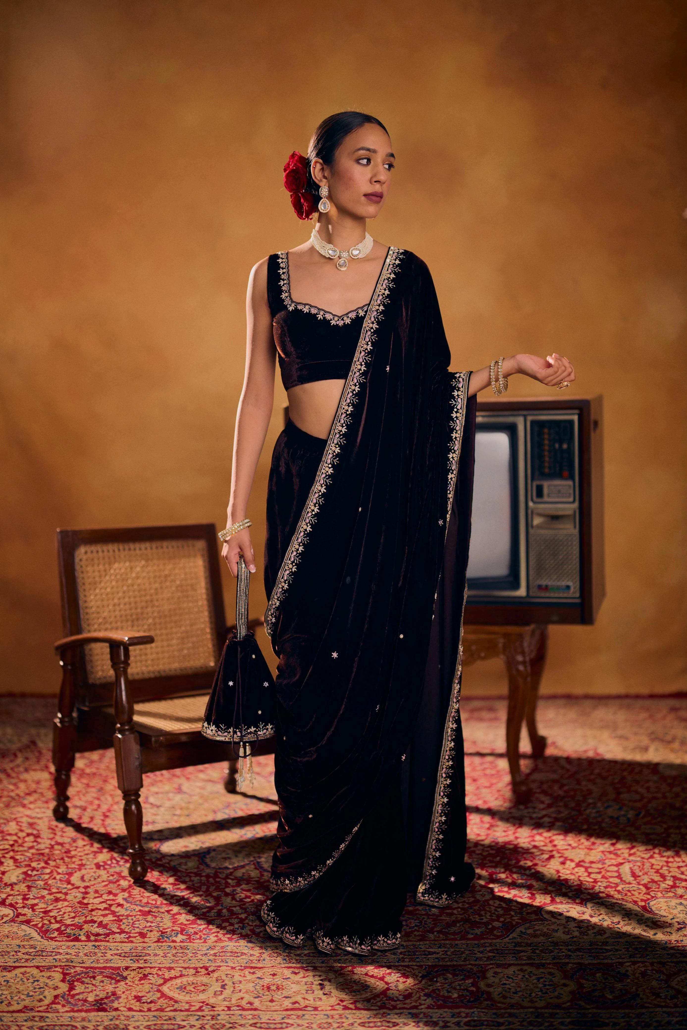 Woman in a black saree with a floral hair accessory in an indoor setting.