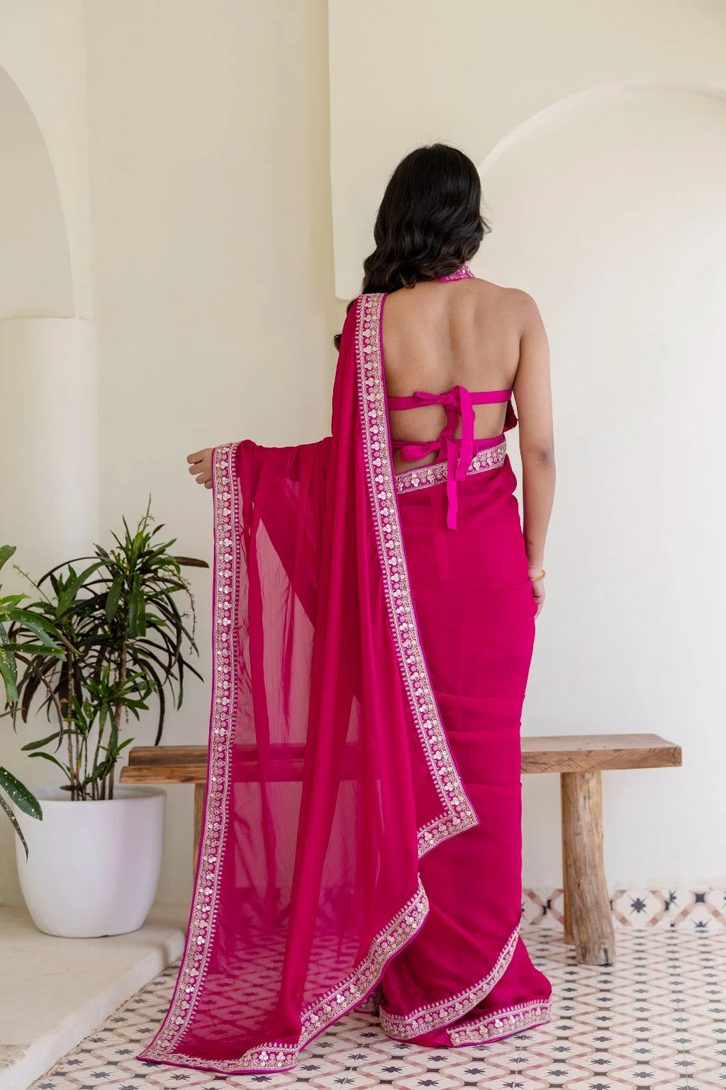 Woman wearing a bright pink saree with a white border in an indoor setting.